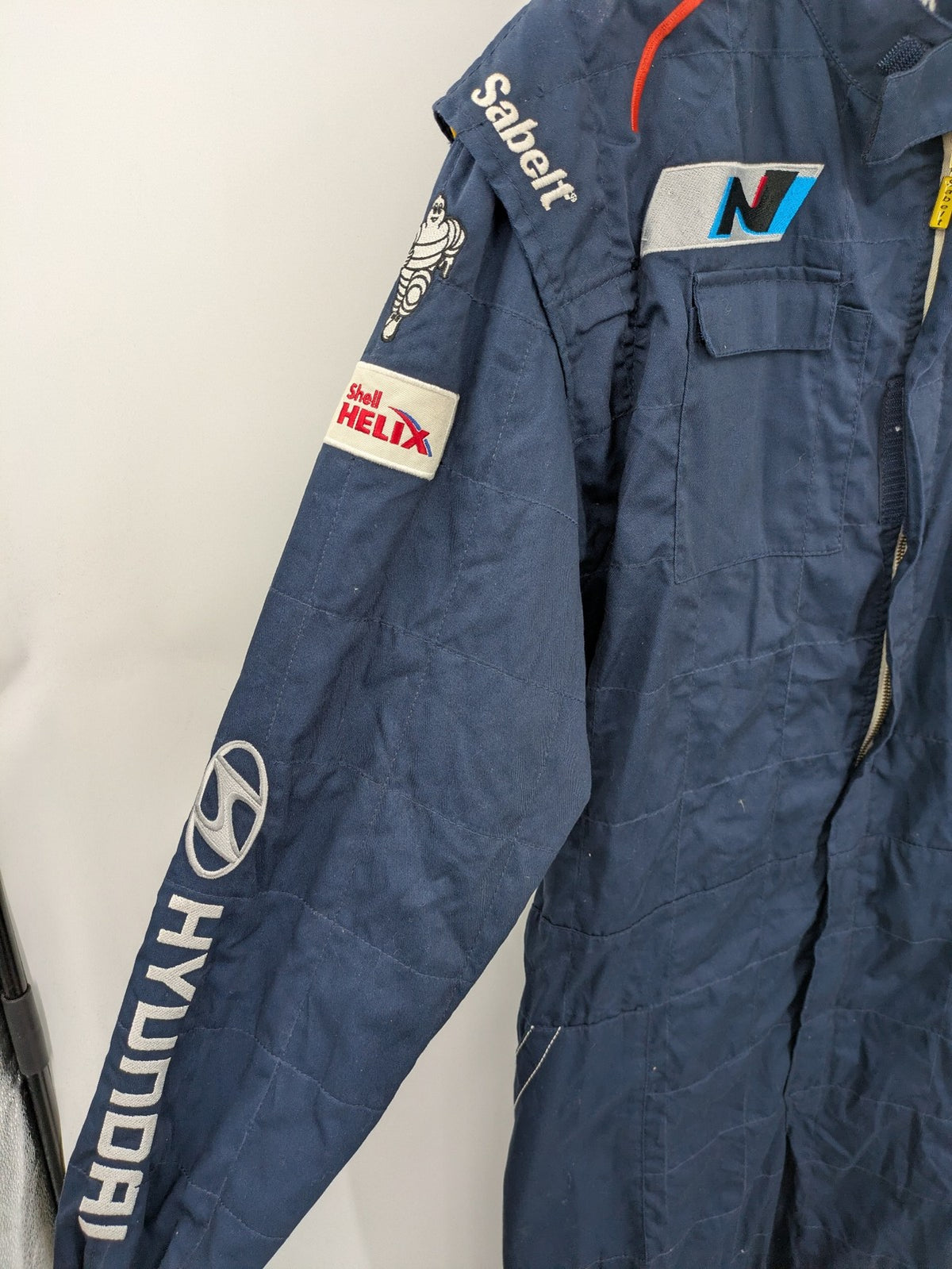 Hyundai Motorsport Sabelt racing suit navy blue with embroidered Shell and Michelin logos.