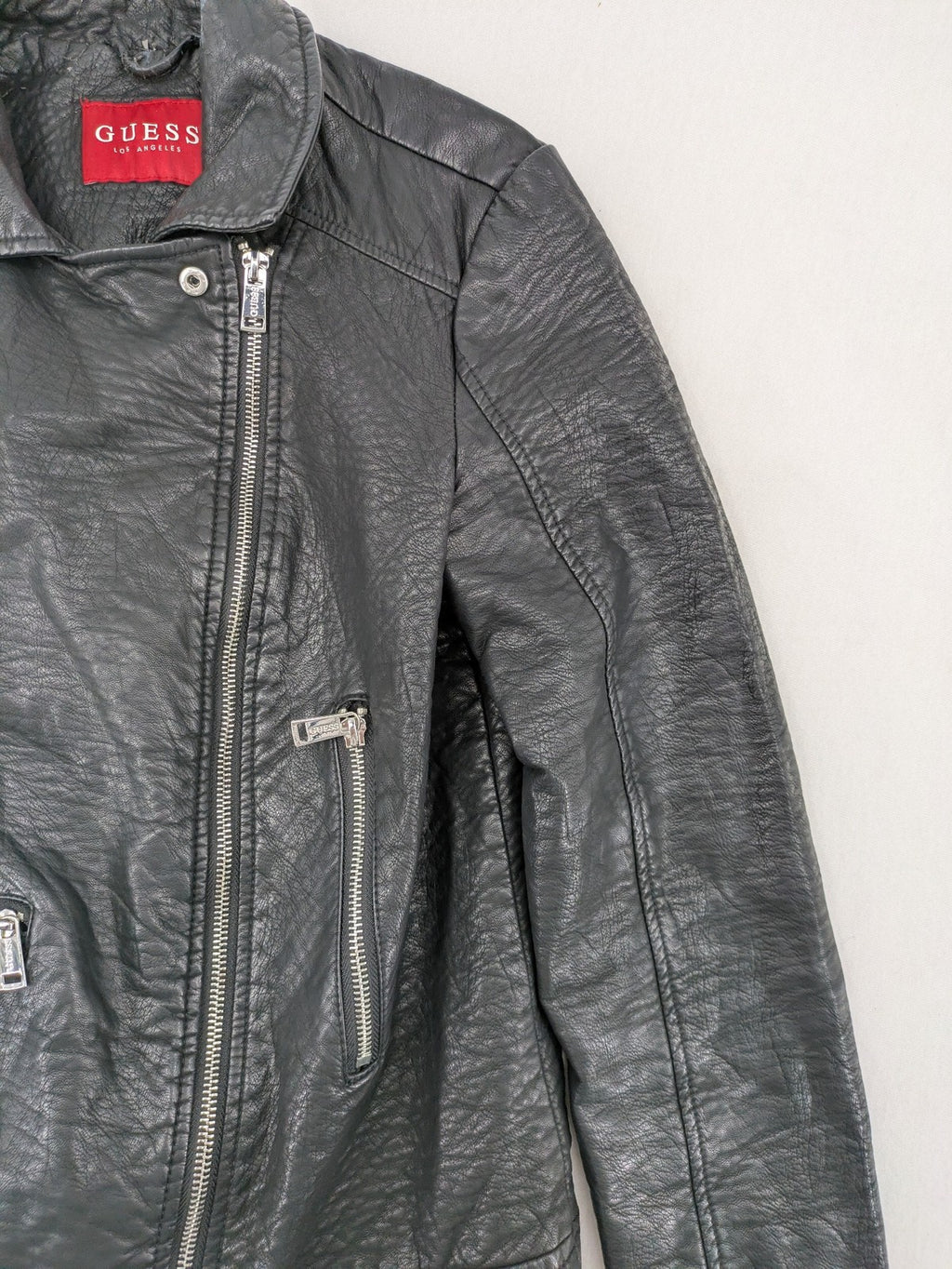 Guess black faux leather biker jacket with asymmetric zipper and multiple zip pockets.
