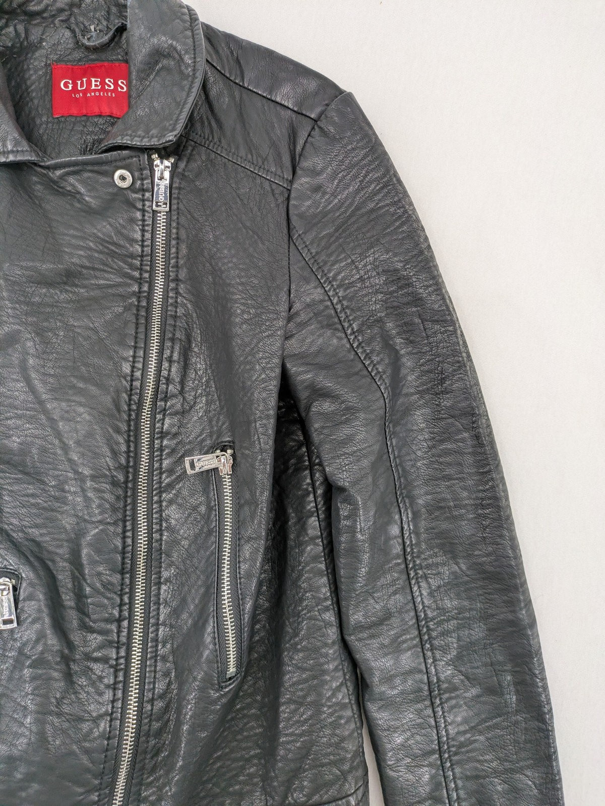 Guess black faux leather biker jacket with asymmetric zipper and multiple zip pockets.