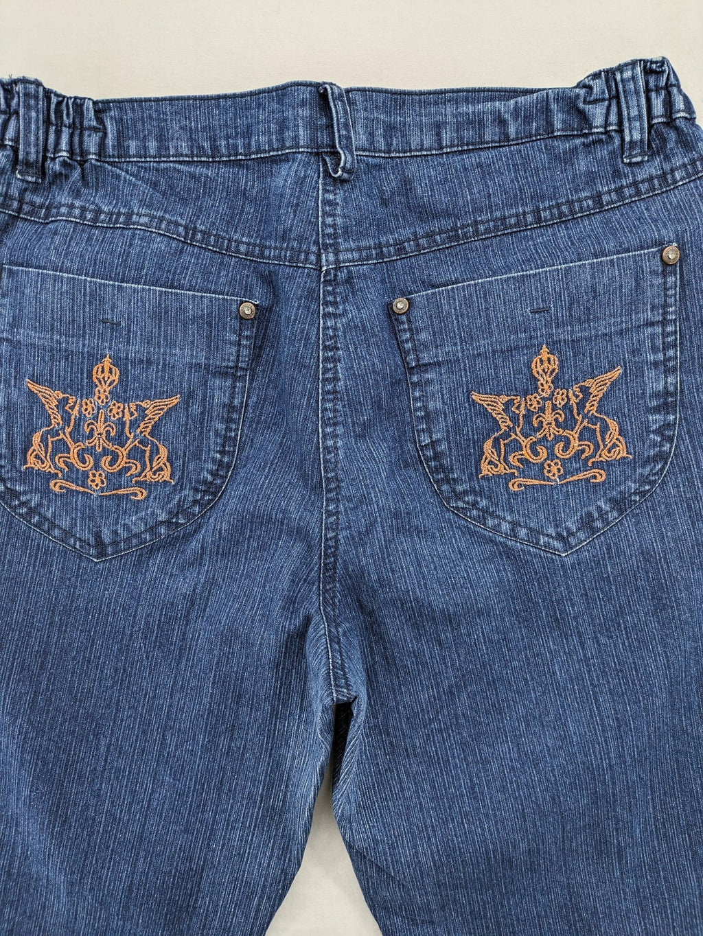 Outfit blue straight jeans with elastic waistband and embroidered crown-wing emblem on pockets.