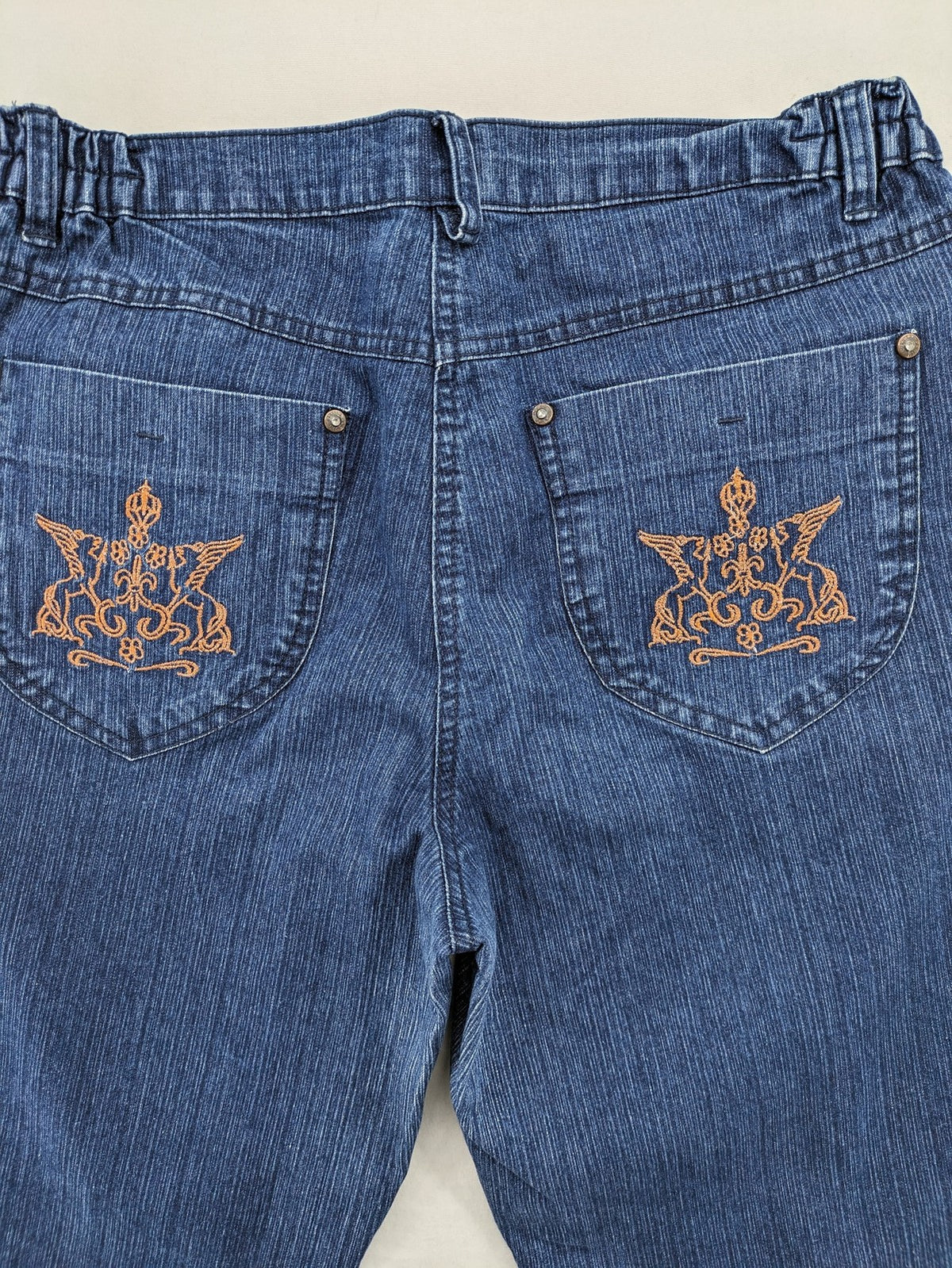 Outfit blue straight jeans with elastic waistband and embroidered crown-wing emblem on pockets.