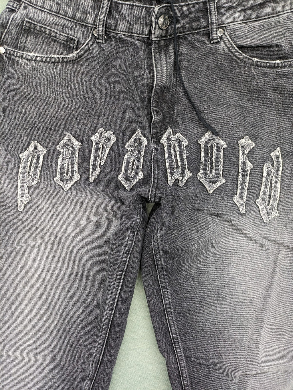 Black Squad black straight jeans with Gothic "Paranoid" lettering and faded finish.
