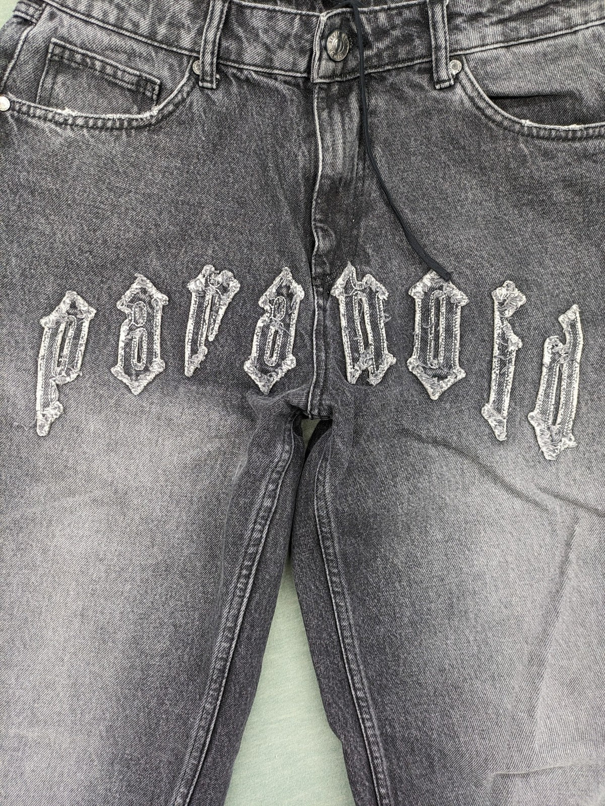 Black Squad black straight jeans with Gothic "Paranoid" lettering and faded finish.