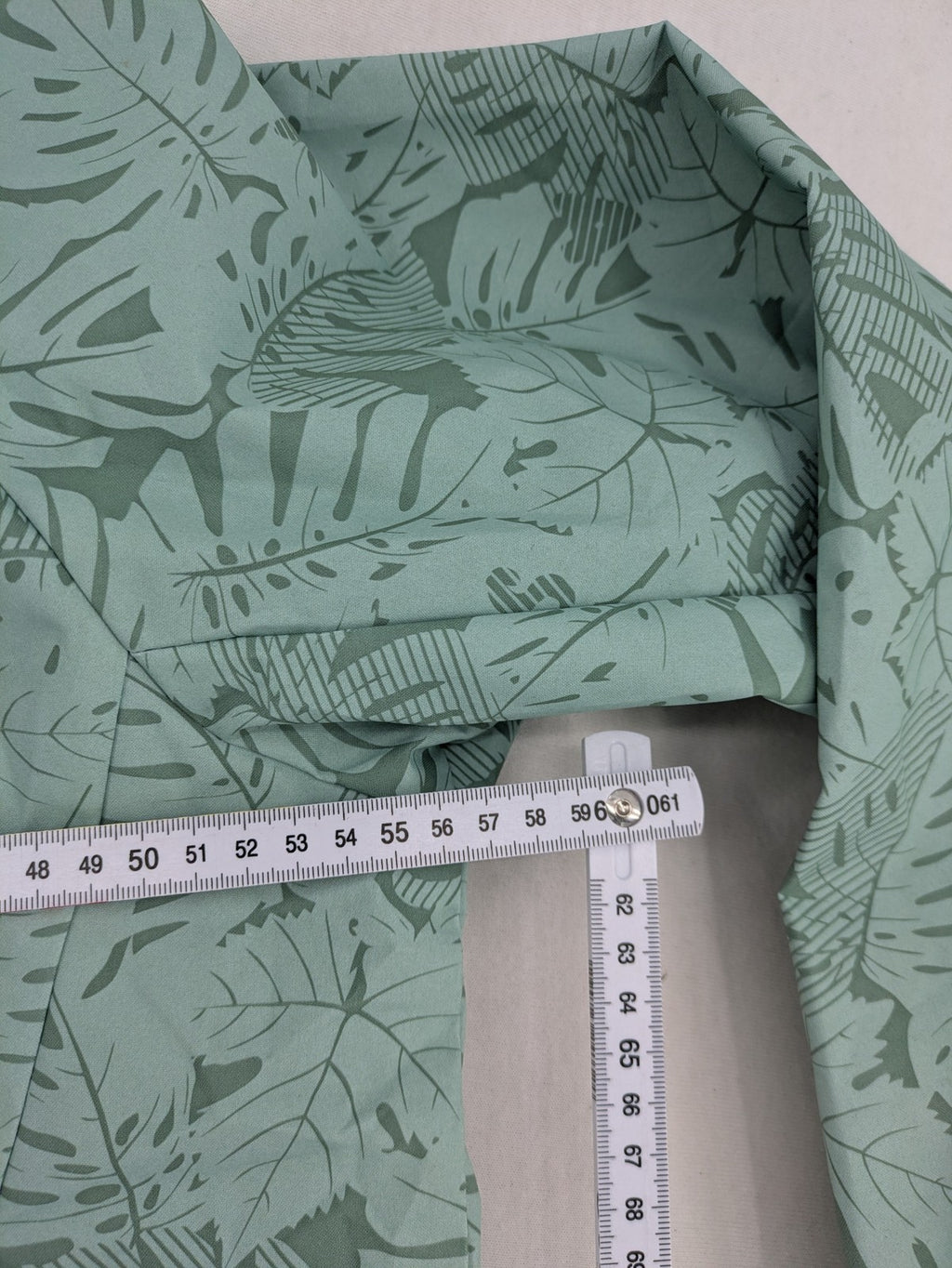 Outdoor green jacket with allover leaf print, adjustable hood, and front zipper.