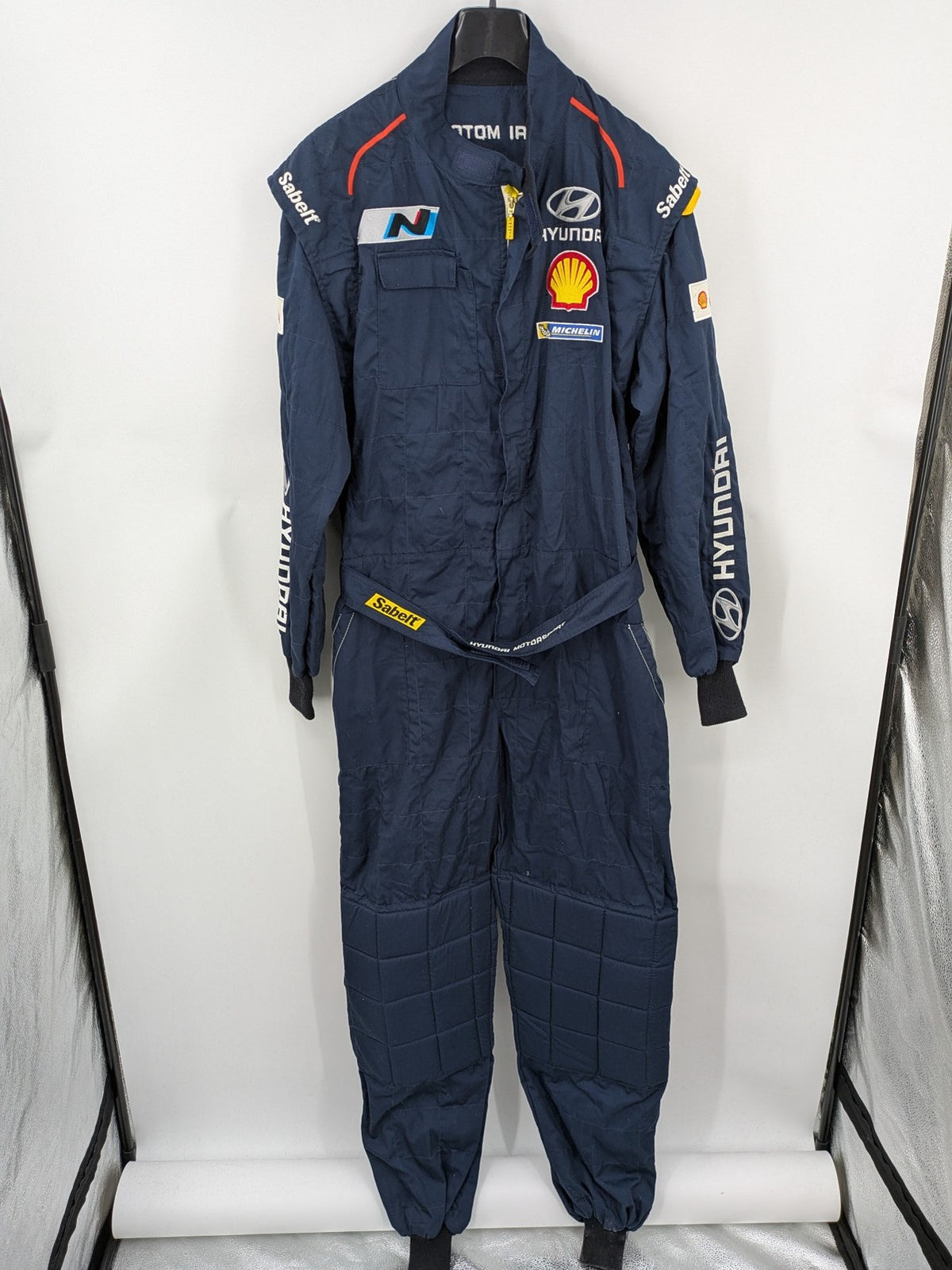 Hyundai Motorsport Sabelt racing suit navy blue with embroidered Shell and Michelin logos.