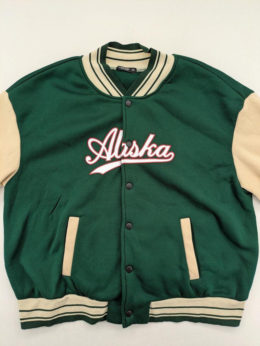 Shein Curve beige bomber jacket with green "Alaska" embroidery and striped ribbed cuffs.