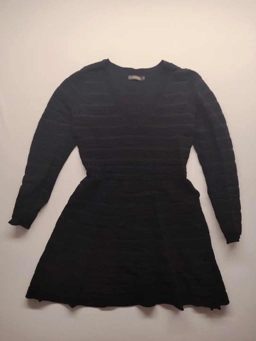 Supertuga black ribbed dress with V-neck, long sleeves, and pointelle detail at waist.