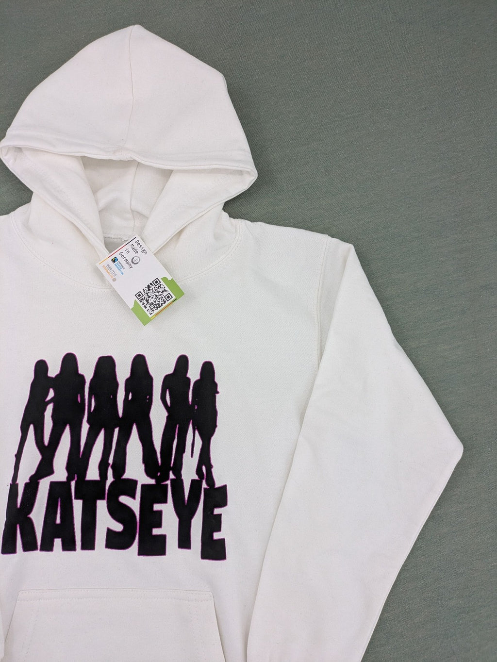 KATSEYE white zip-through hoodie with black silhouette graphic and logo, classic pullover style.