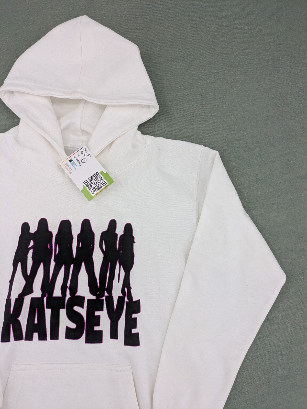 KATSEYE white zip-through hoodie with black silhouette graphic and logo, classic pullover style.
