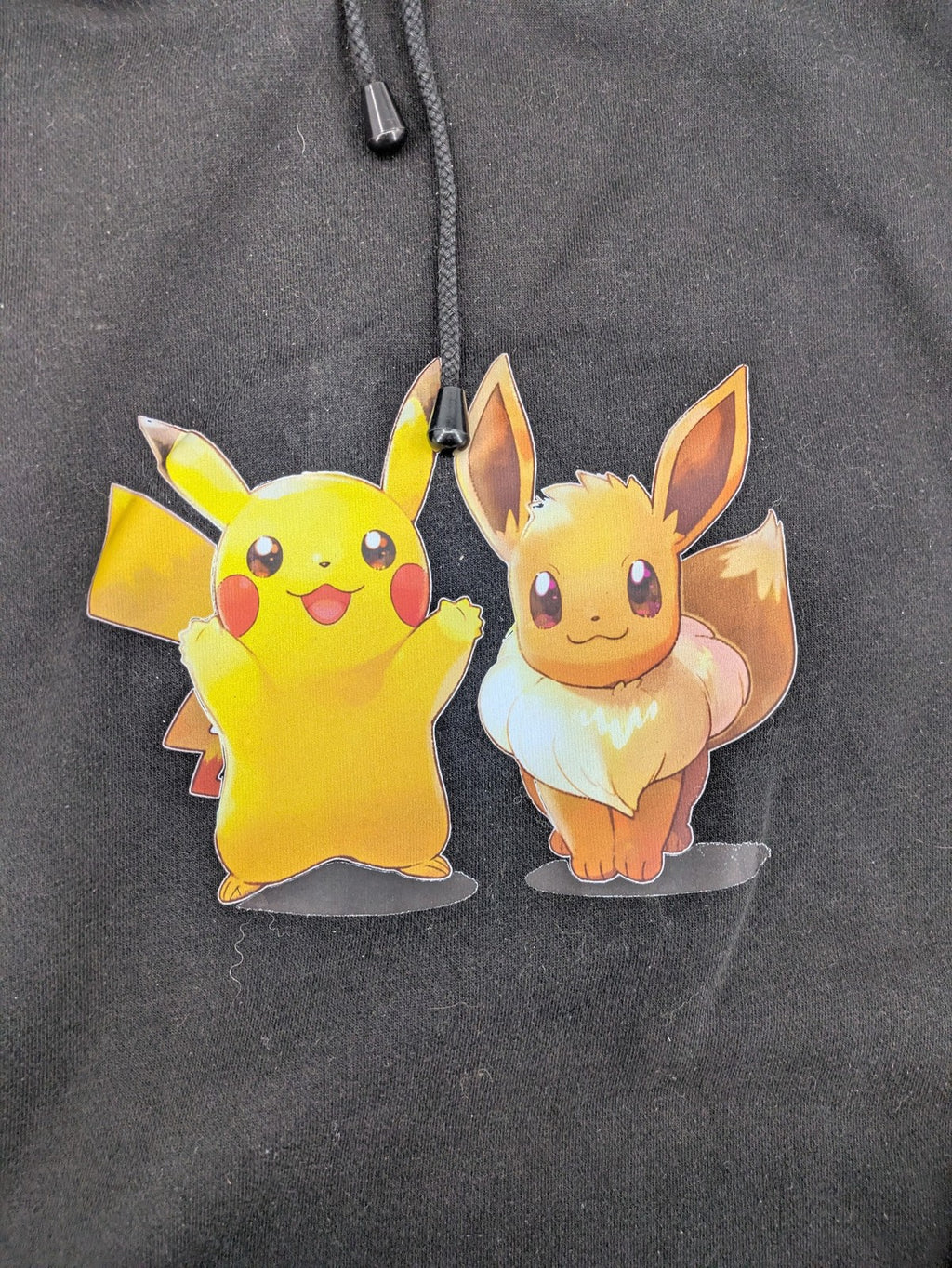 Pokémon black hoodie featuring colorful Pikachu and Evoli graphic, classic pullover style.