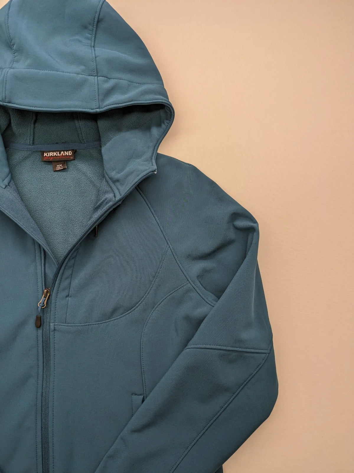 Kirkland Signature blue softshell jacket with hood, fleece lining, and zippered pockets.