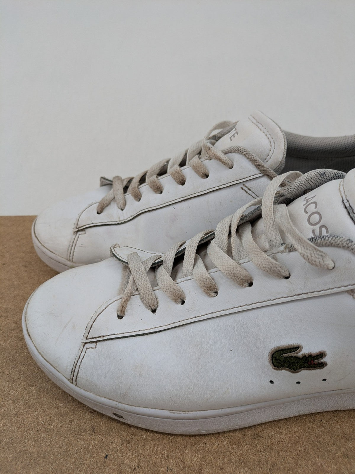 Lacoste cream low top sneakers with iconic crocodile logo and classic design.