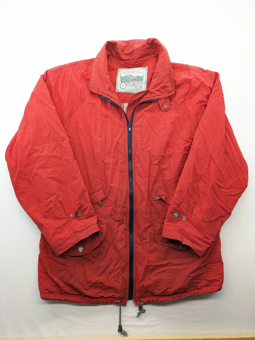 Bush Sportswear red trekking jacket with front zipper, multiple pockets, and striped lining.