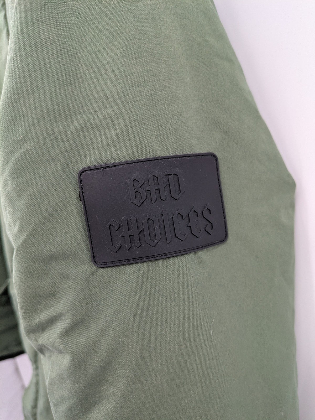Bad Choices green parka coat with reflective details and logo patch on sleeve.