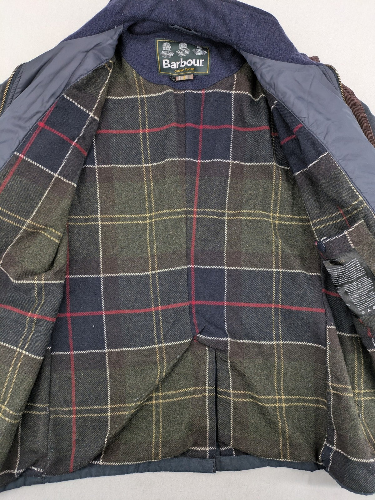 Barbour navy wax jacket with quilted lining and leather elbow patches, tartan interior.