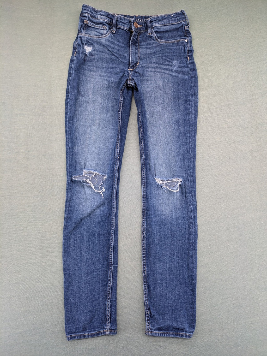 H&M blue skinny jeans with distressed knee details and classic 5-pocket design.