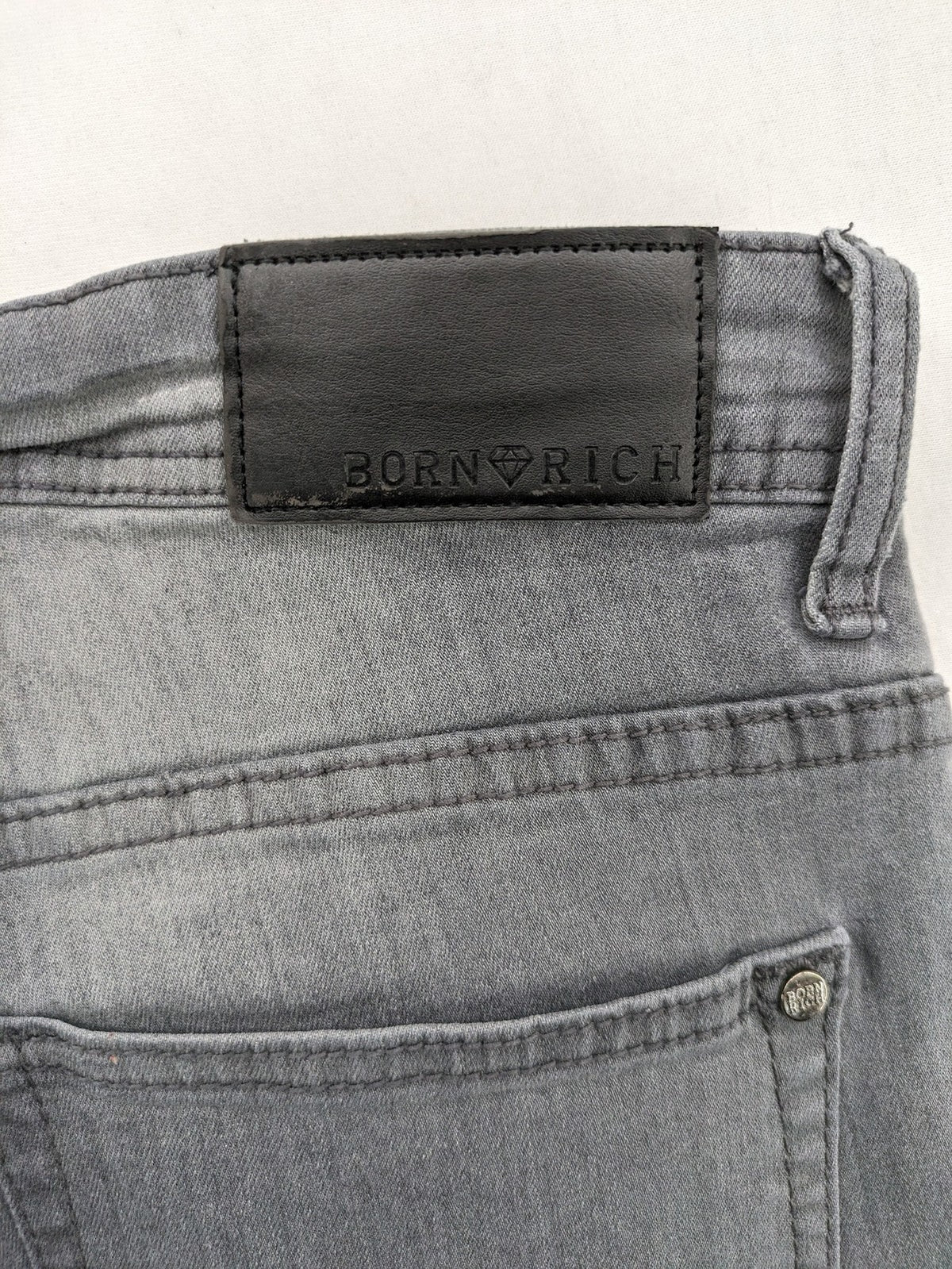 Born Rich grey slim fit jeans with button fly and washed denim texture.