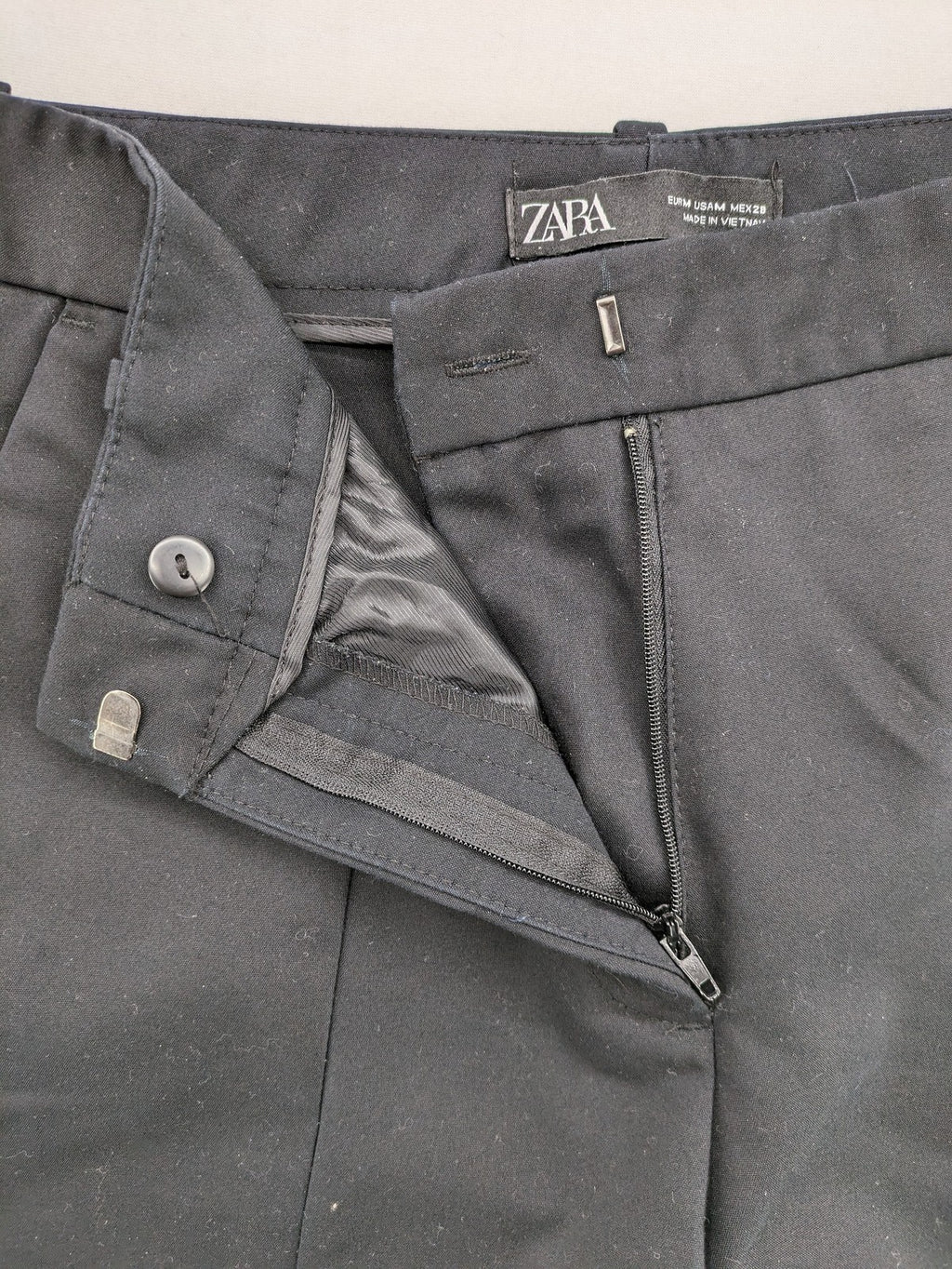 Zara black pants with front creases, subtle slit hem, and buttoned back pocket.