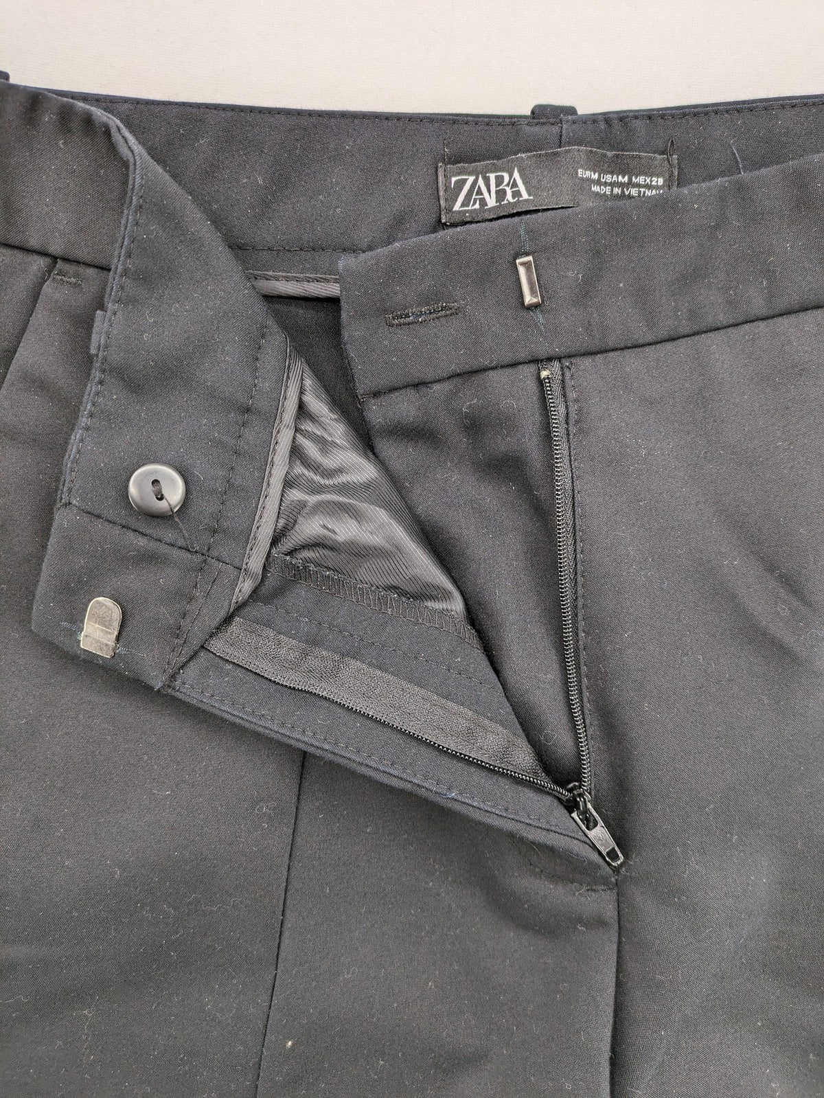 Zara black pants with front creases, subtle slit hem, and buttoned back pocket.