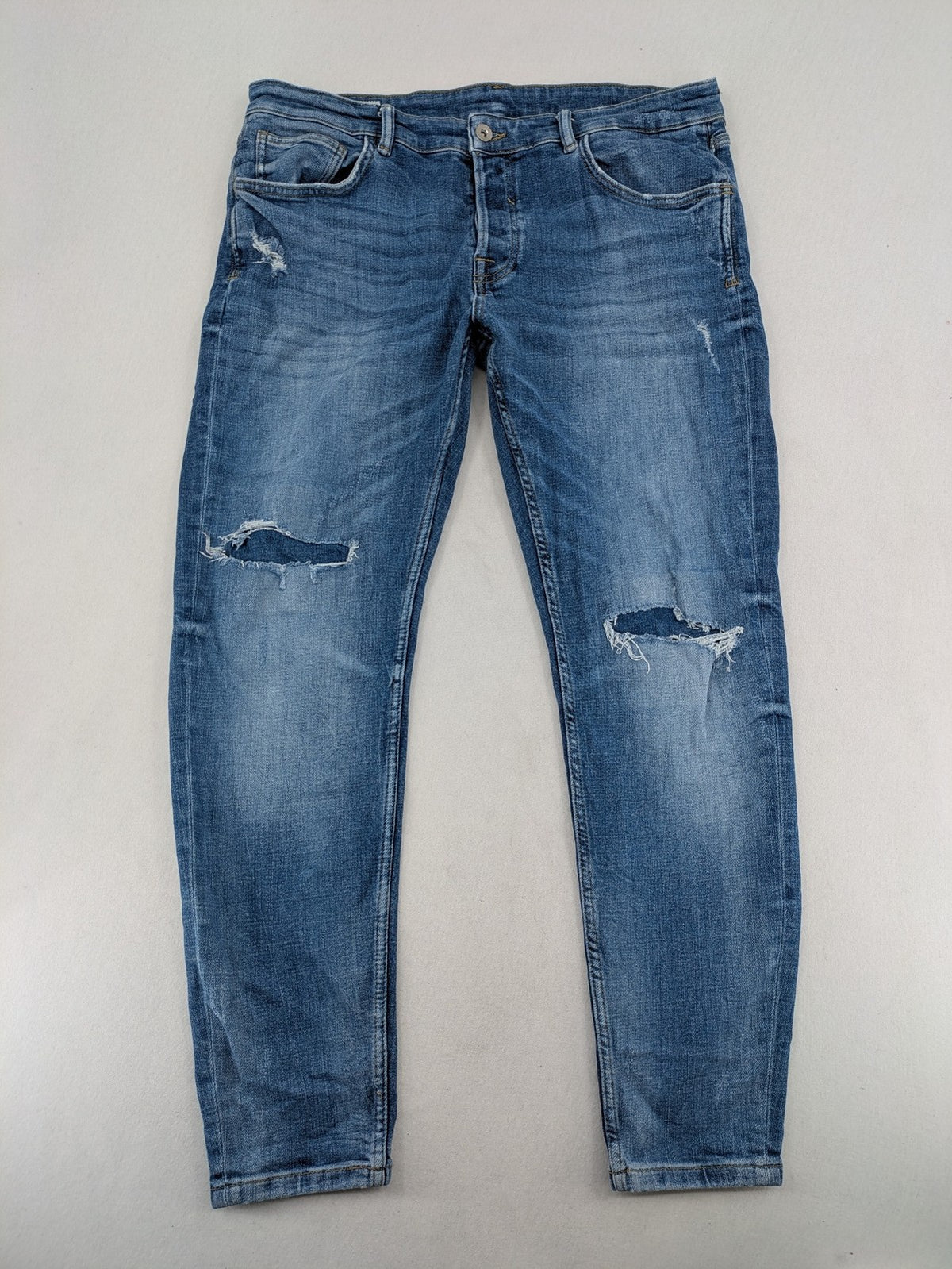 Zara blue straight jeans with distressed ripped knees and button-fly closure.