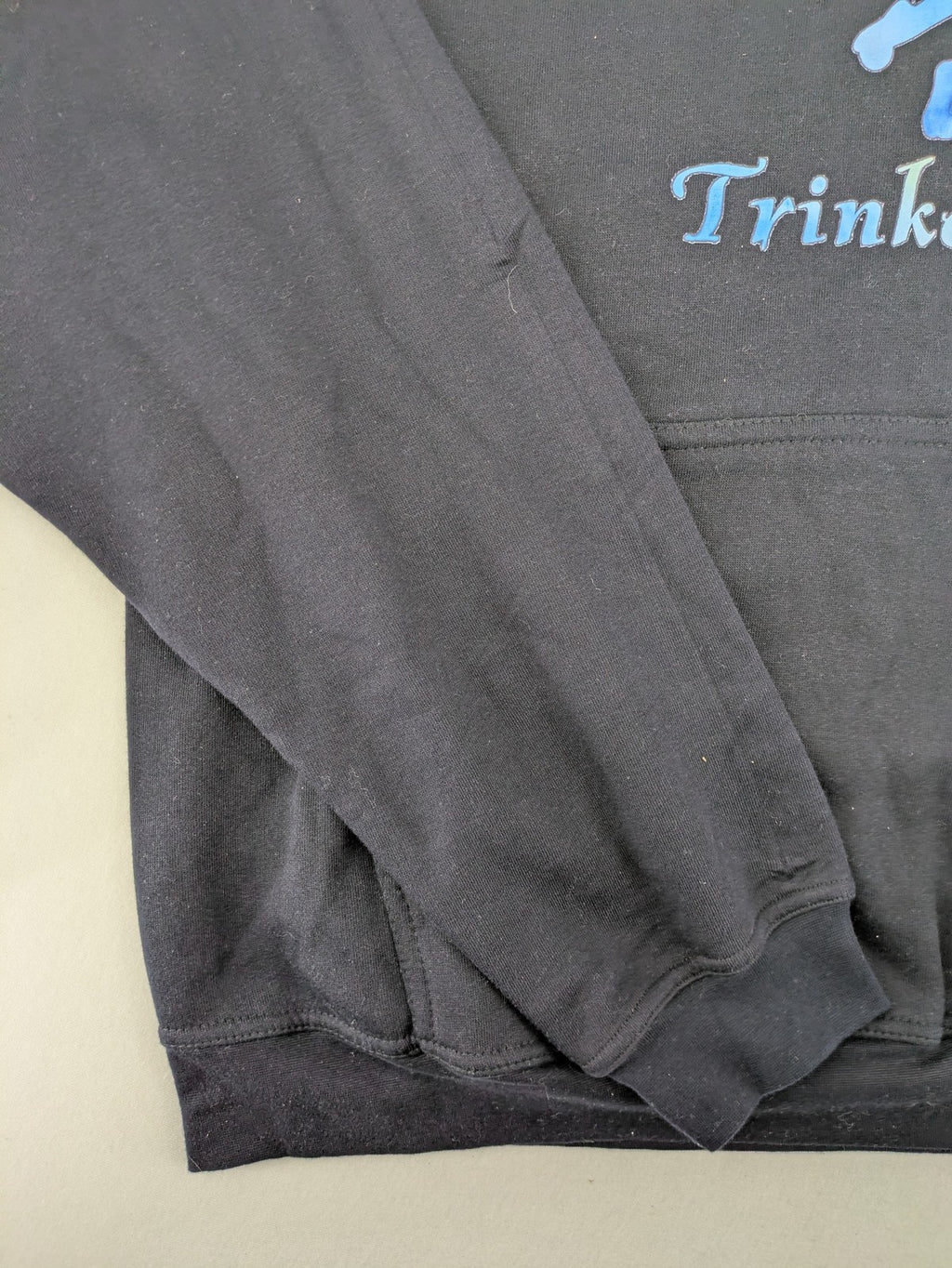 Trinkerbell black zip-through hoodie with blue graphic and adjustable drawstring hood.