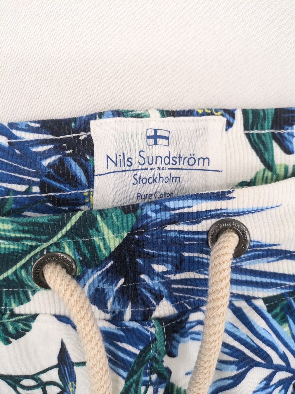 Nils Sundström blue and green tropical floral shorts with white background and elastic waistband.