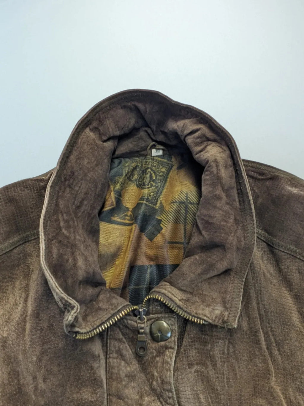Vintage brown leather jacket with graphic lining, zip closure, and button placket.