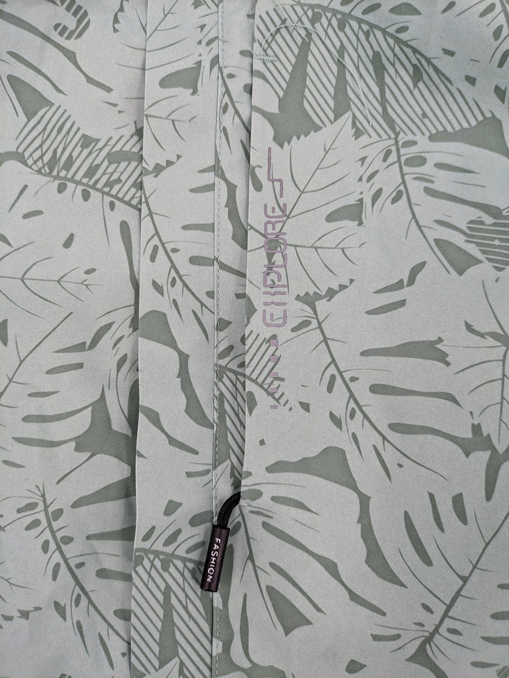 Outdoor green jacket with allover leaf print, adjustable hood, and front zipper.