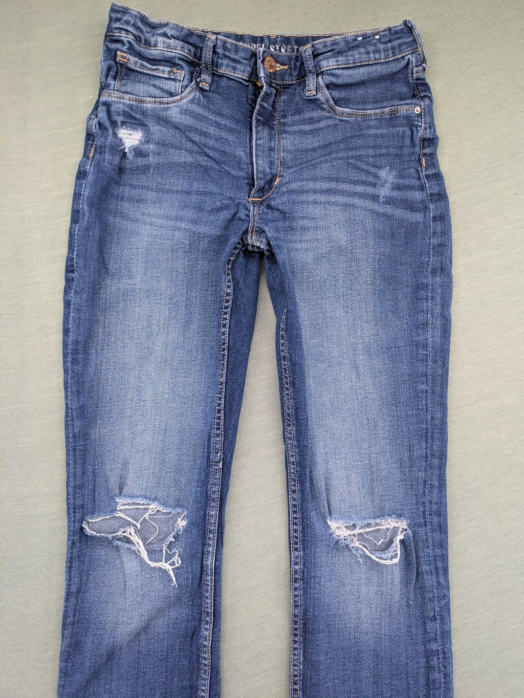H&M blue skinny jeans with distressed knee details and classic 5-pocket design.