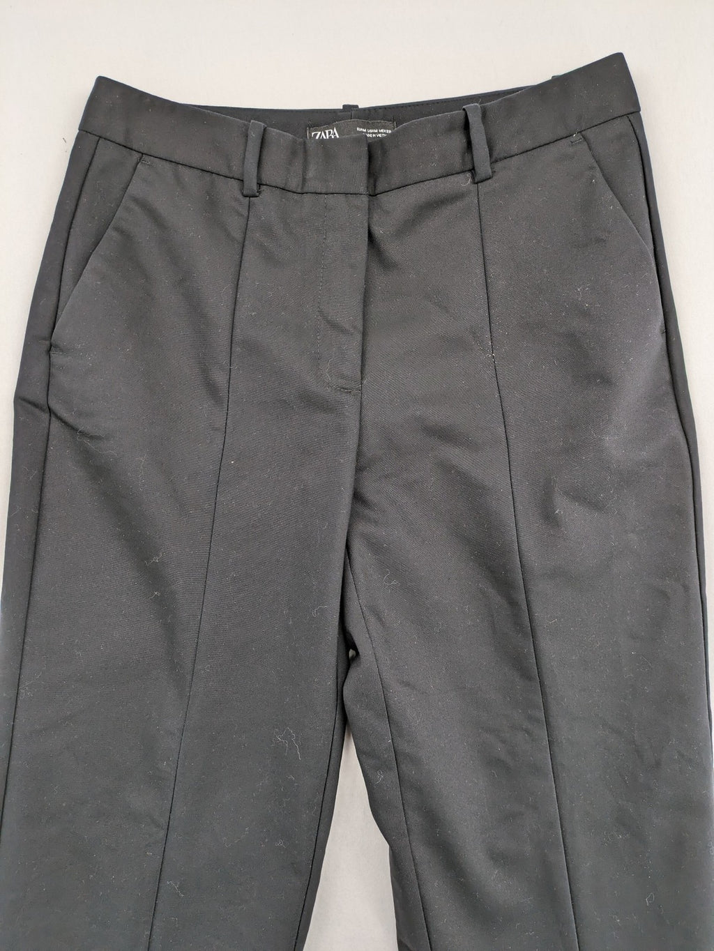 Zara black pants with front creases, subtle slit hem, and buttoned back pocket.