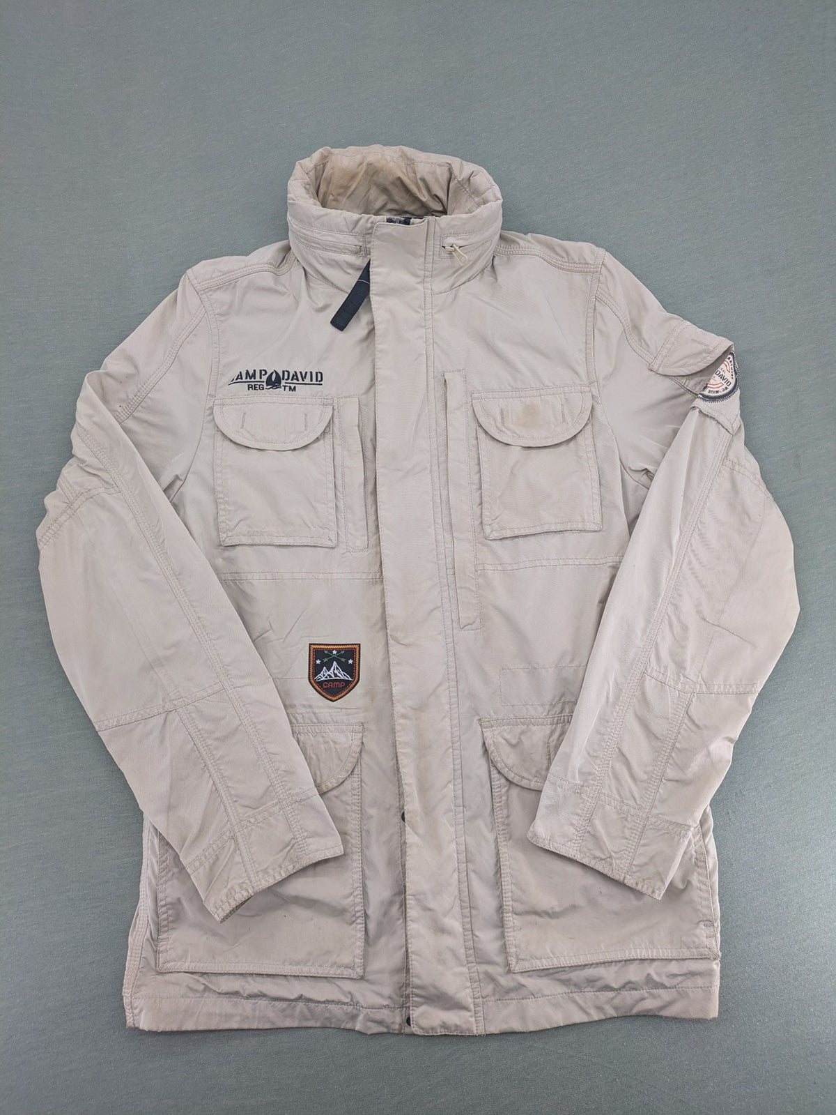 Camp David beige field jacket with logo patches, standing collar, and multiple pockets.