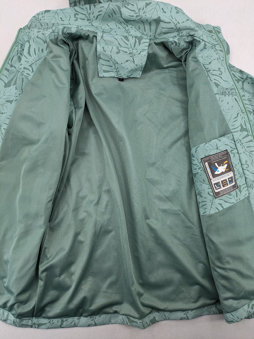 Outdoor green jacket with allover leaf print, adjustable hood, and front zipper.