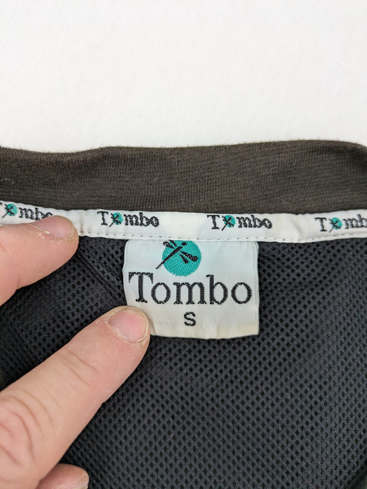 Tombo green windbreaker jacket with white piping, V-neck, and zippered pockets.