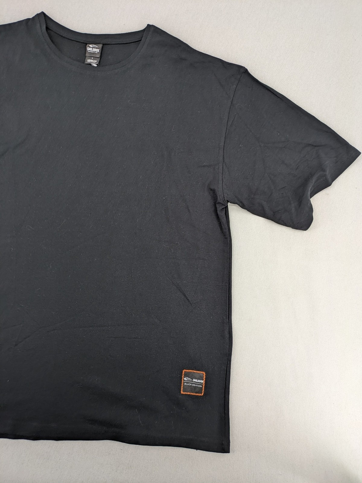 Smilodox black T-shirt minimalist design with subtle brand patch, 100% cotton.
