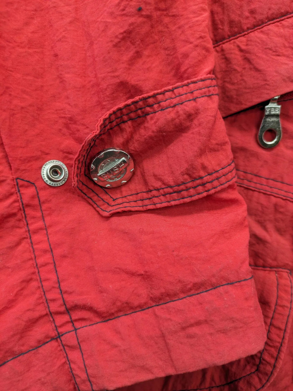 Bush Sportswear red trekking jacket with front zipper, multiple pockets, and striped lining.