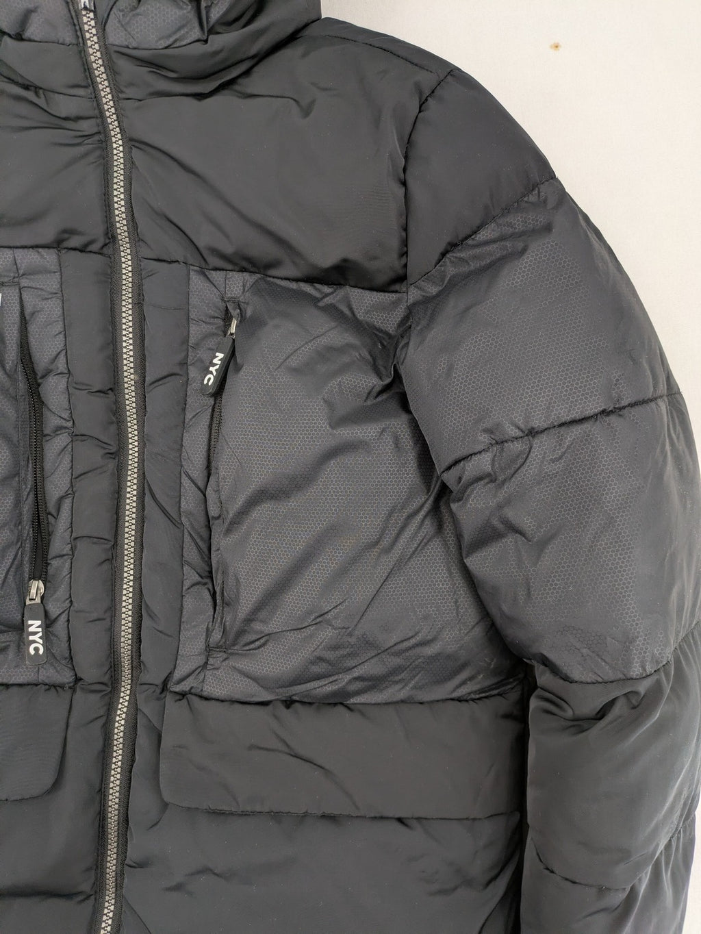 C&A black puffer jacket with NYC83 graphic, hood, and multiple pockets.