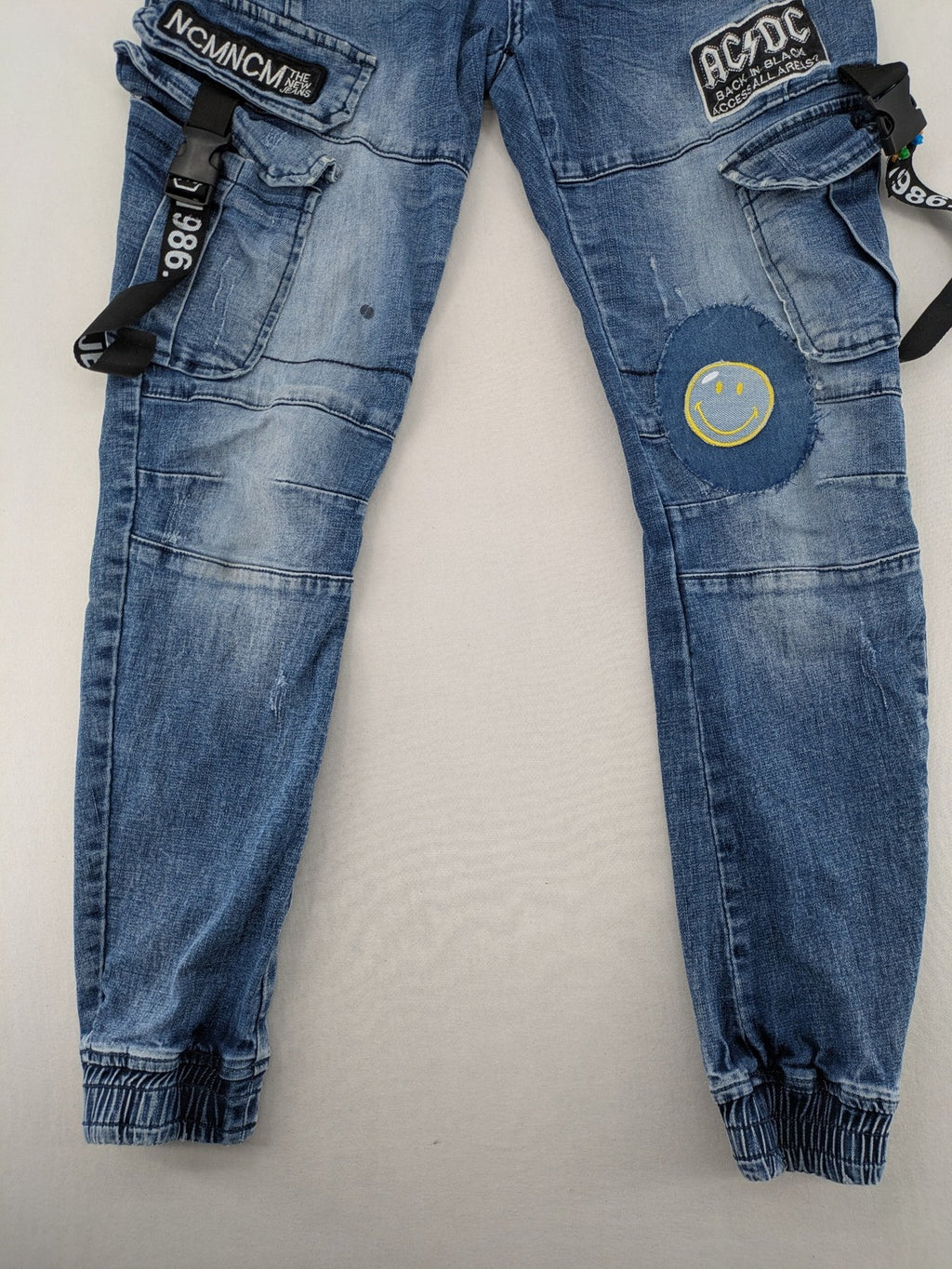 FN.G blue straight jeans with AC/DC patch, smiley face, and elastic jogger cuffs.
