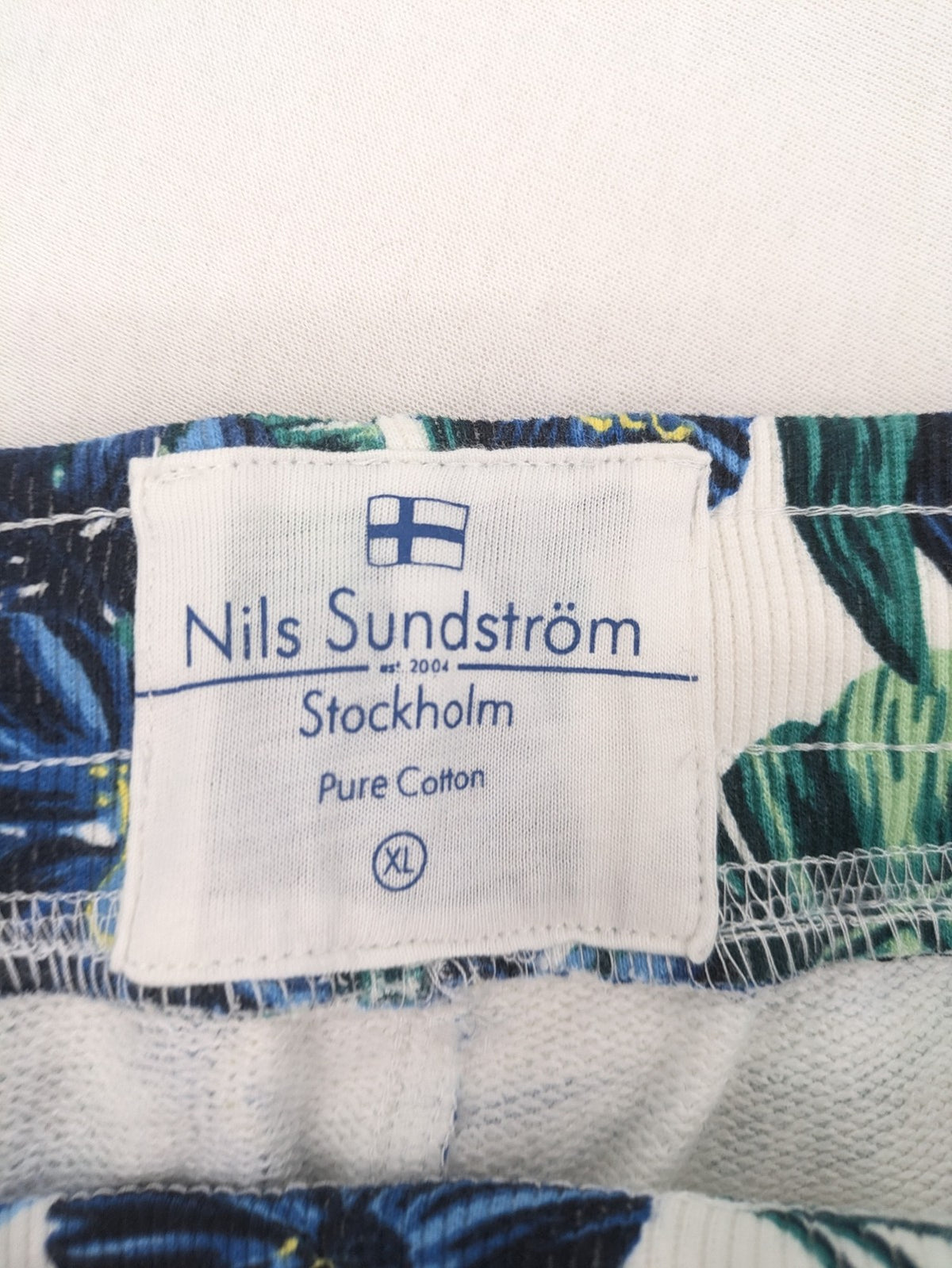 Nils Sundström blue and green tropical floral shorts with white background and elastic waistband.