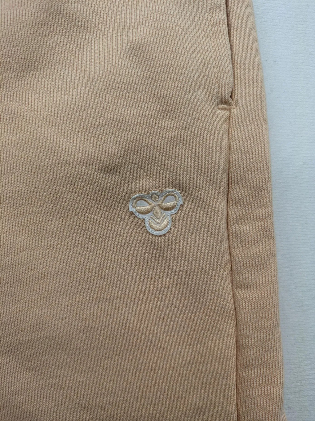 Hummel beige jogging pants with adjustable drawstring, embroidered logo, and ankle cuffs.