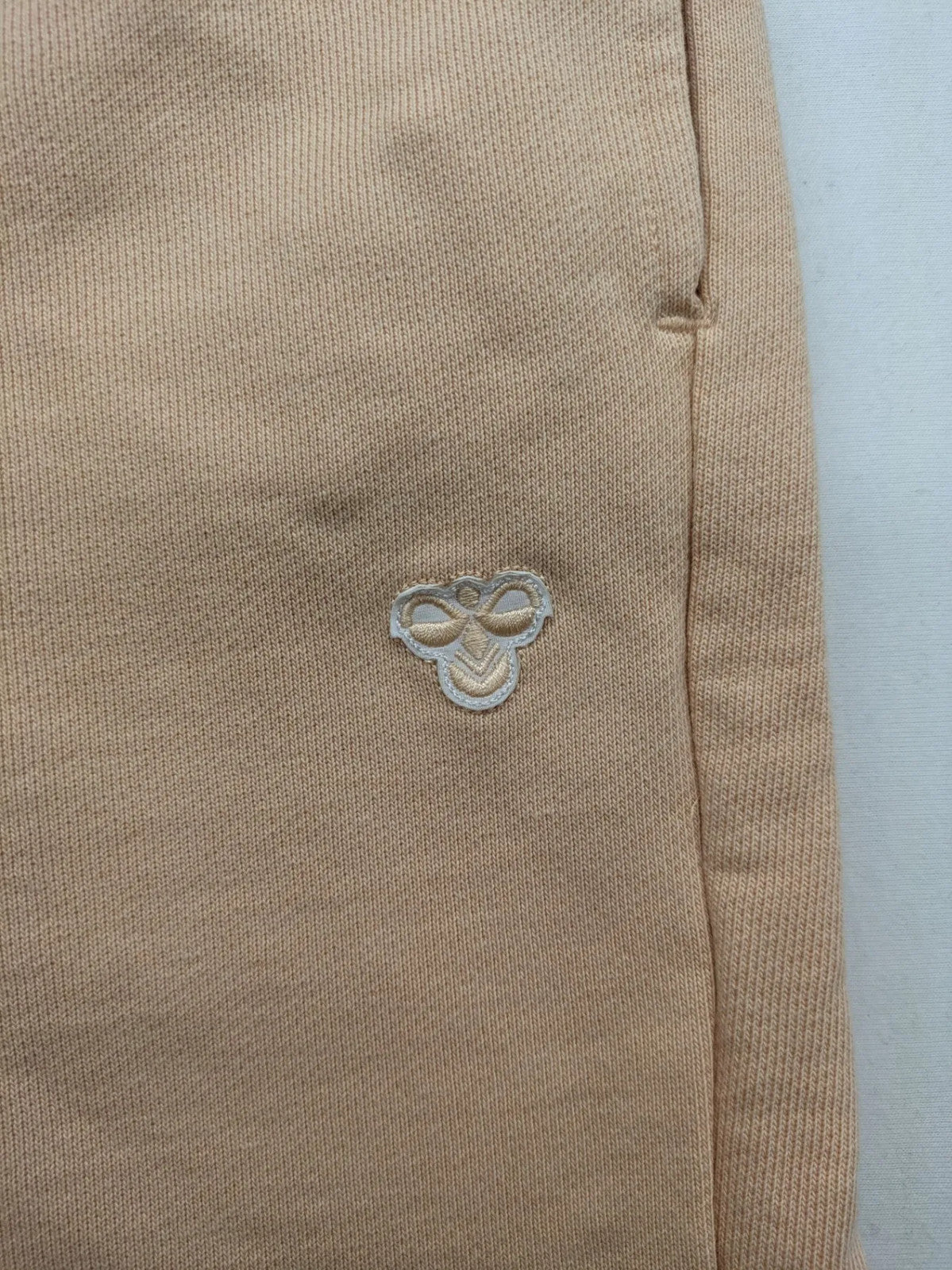 Hummel beige jogging pants with adjustable drawstring, embroidered logo, and ankle cuffs.
