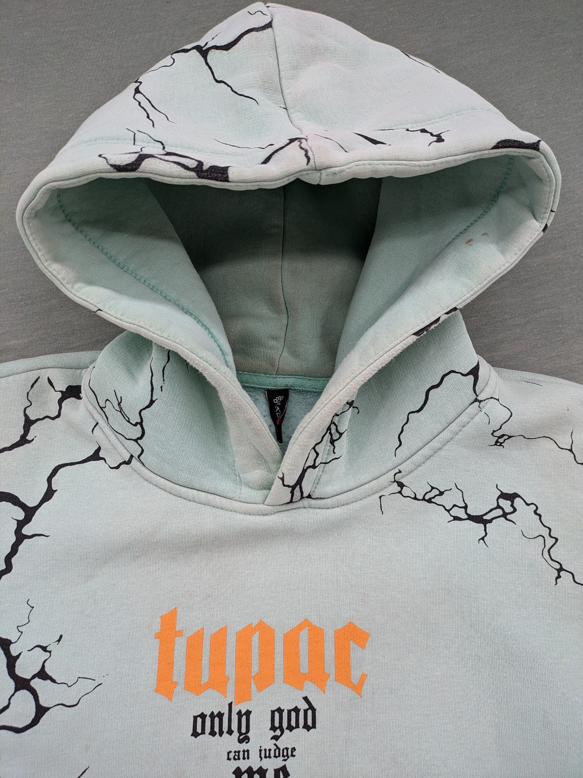 Tupac black and green zip-through hoodie with "Only God Can Judge Me" front print and angel wings graphic.