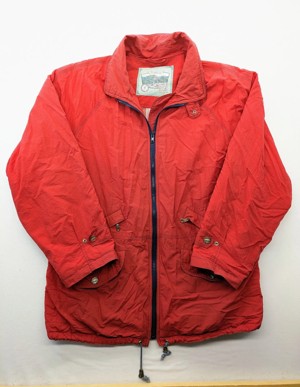 Bush Sportswear red trekking jacket with front zipper, multiple pockets, and striped lining.