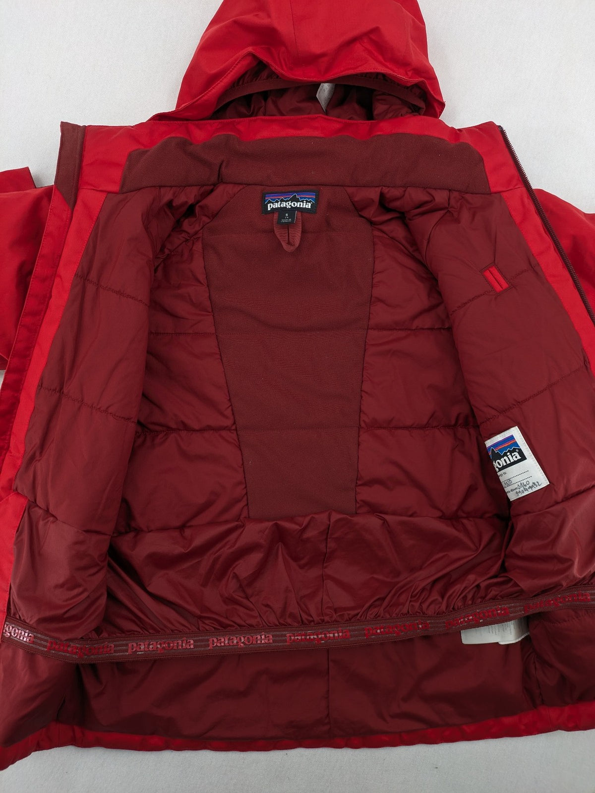 Patagonia red winter coat with hood, zip closure, snow skirt, and ski pass pocket.