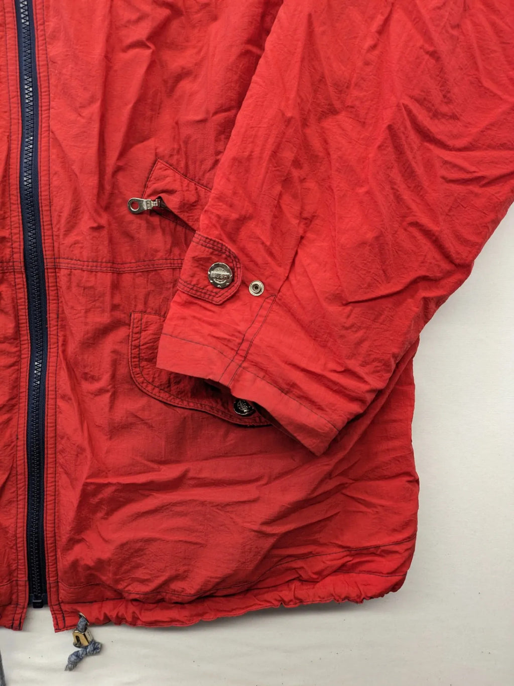 Bush Sportswear red trekking jacket with front zipper, multiple pockets, and striped lining.