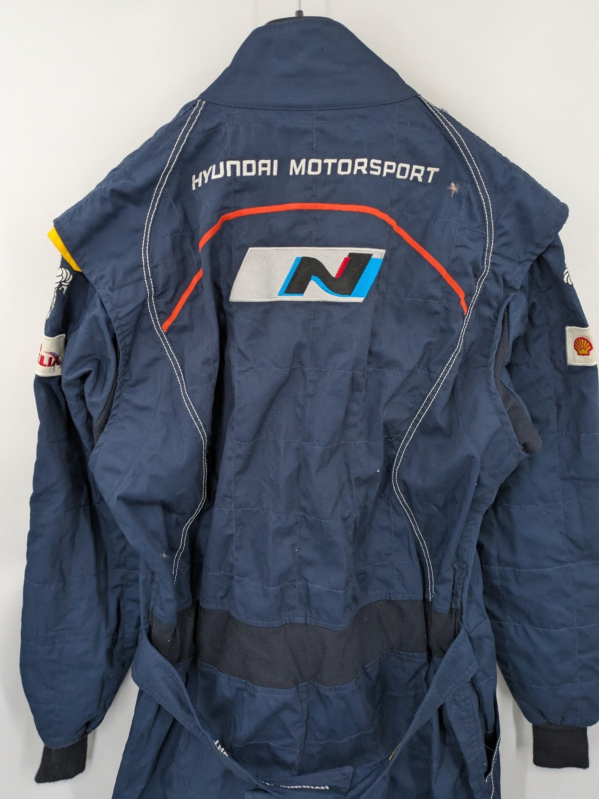 Hyundai Motorsport Sabelt racing suit navy blue with embroidered Shell and Michelin logos.