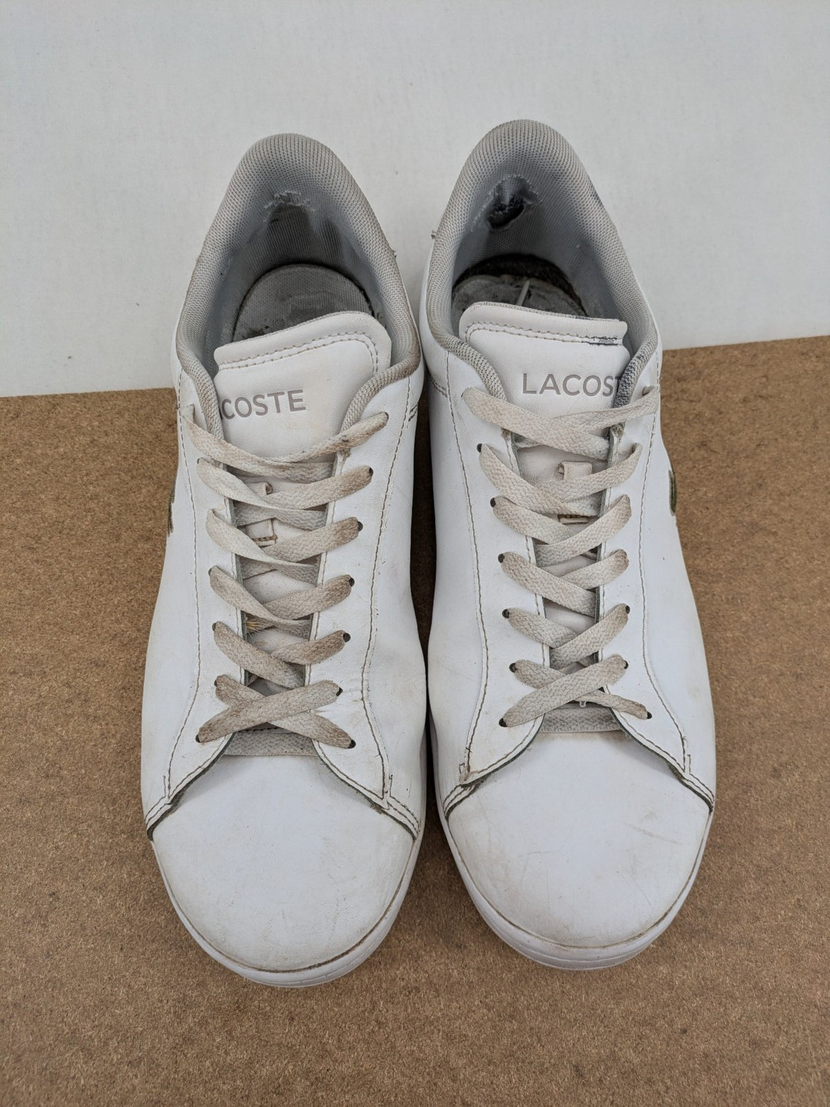 Lacoste cream low top sneakers with iconic crocodile logo and classic design.