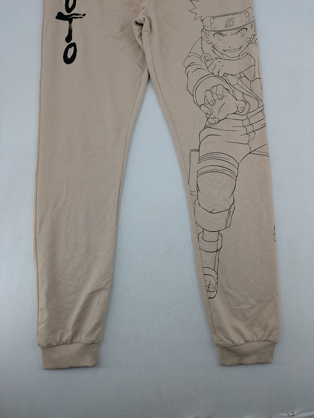 Naruto Shippuden beige joggers featuring Naruto Uzumaki graphic and logo print.