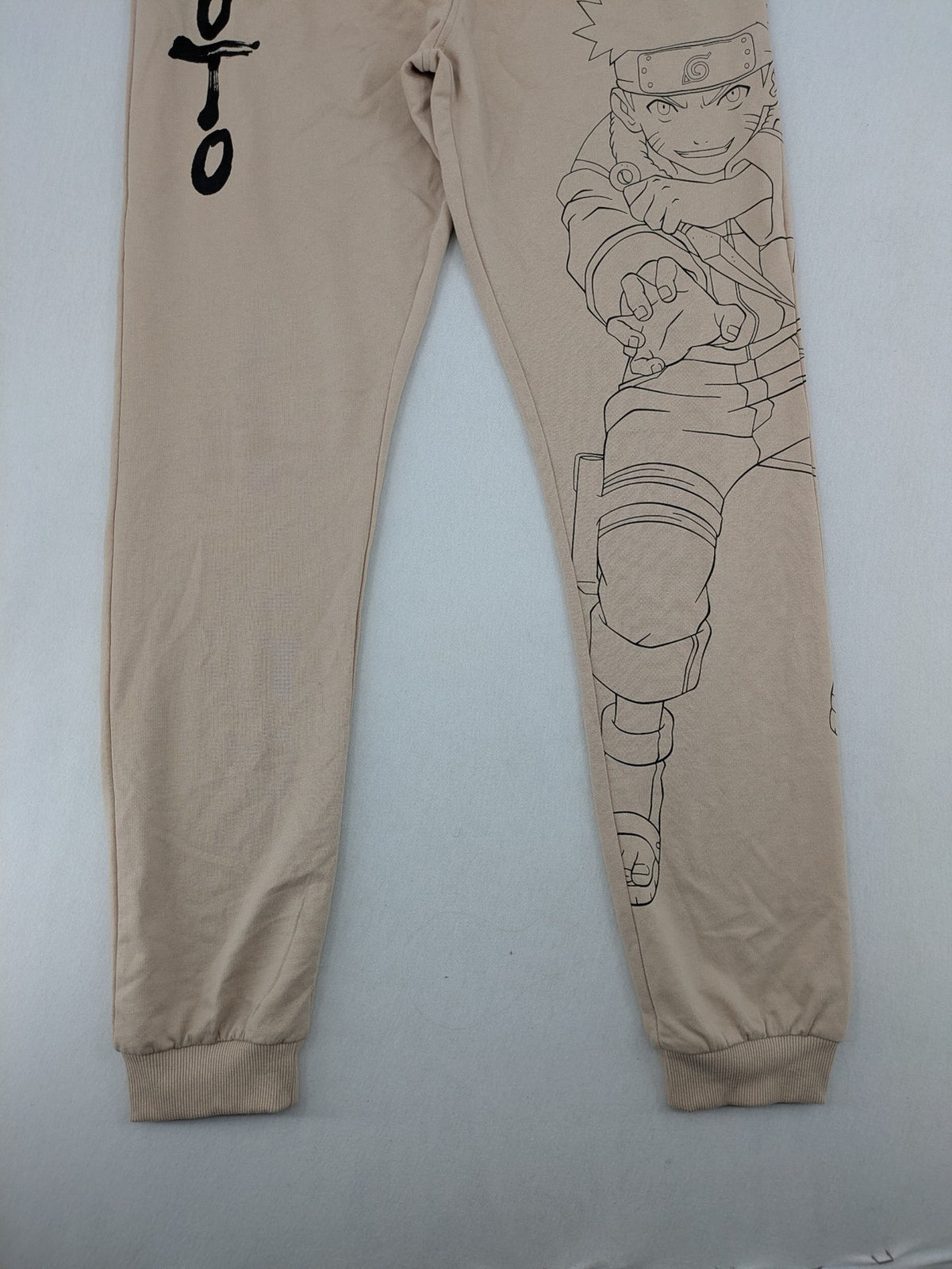 Naruto Shippuden beige joggers featuring Naruto Uzumaki graphic and logo print.