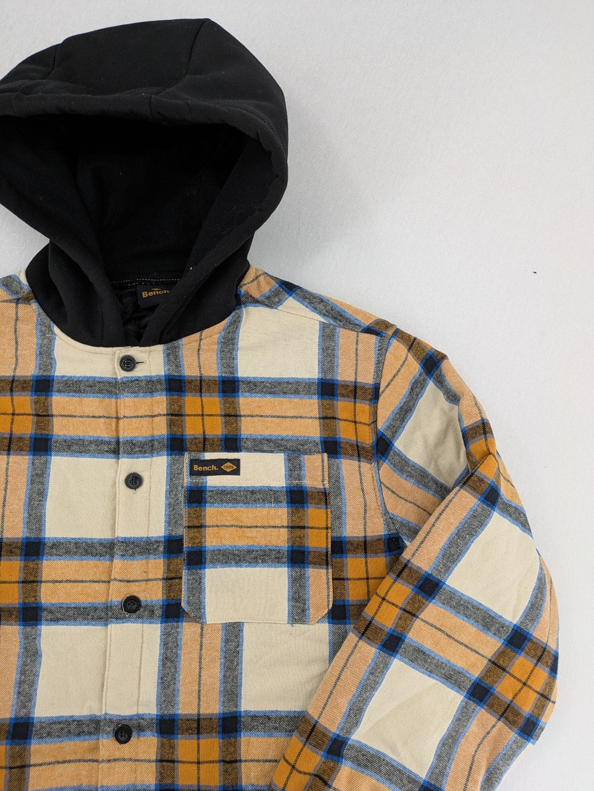 Bench cream flannel jacket with check pattern, black hood, and button placket.