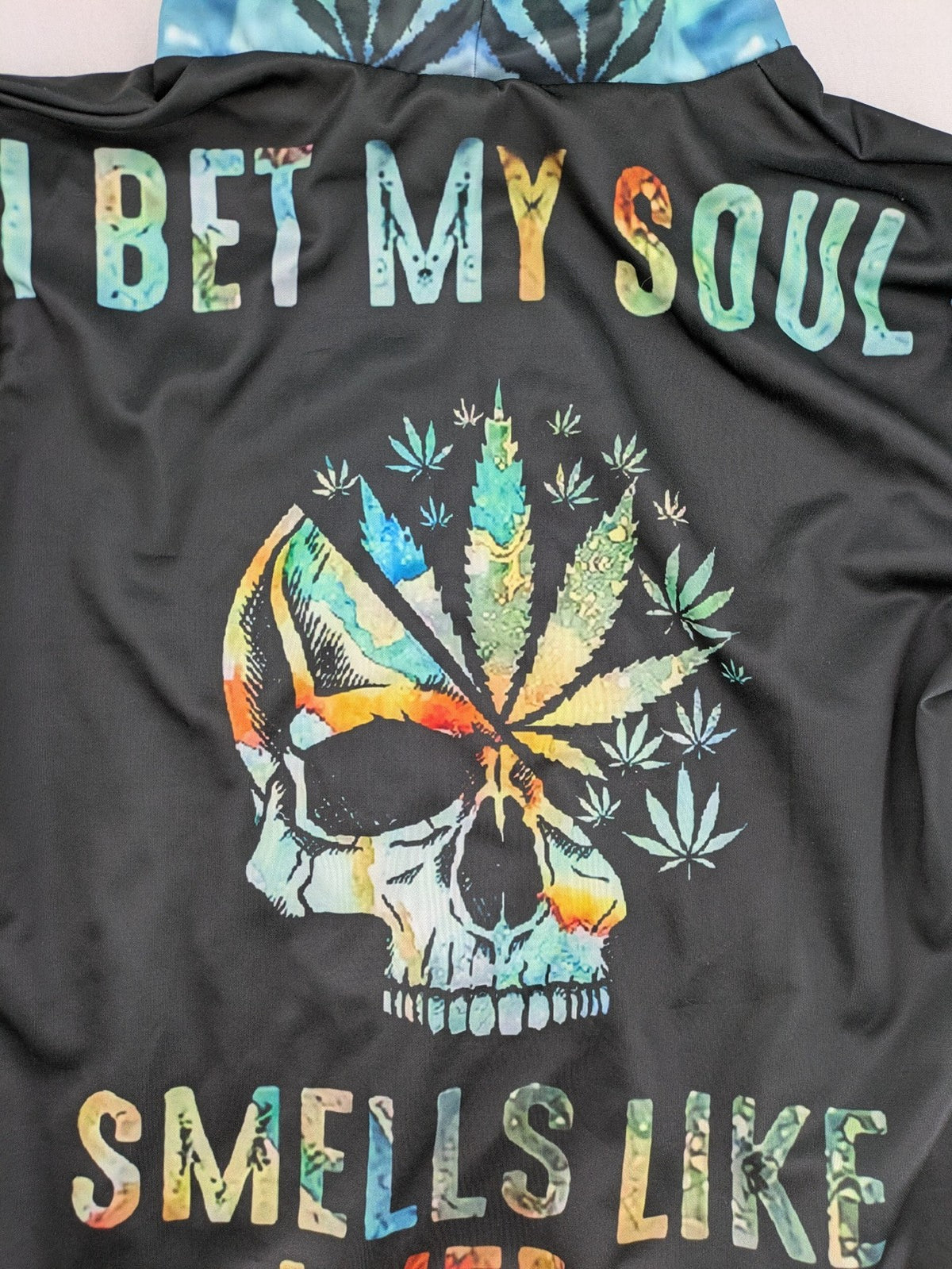 Skull tie-dye hoodie blue green with cannabis leaf graphic and bold text.